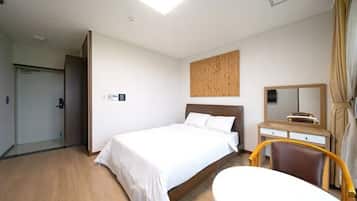A hotel room with a bed, a desk with a chair, a mirror, and a door.