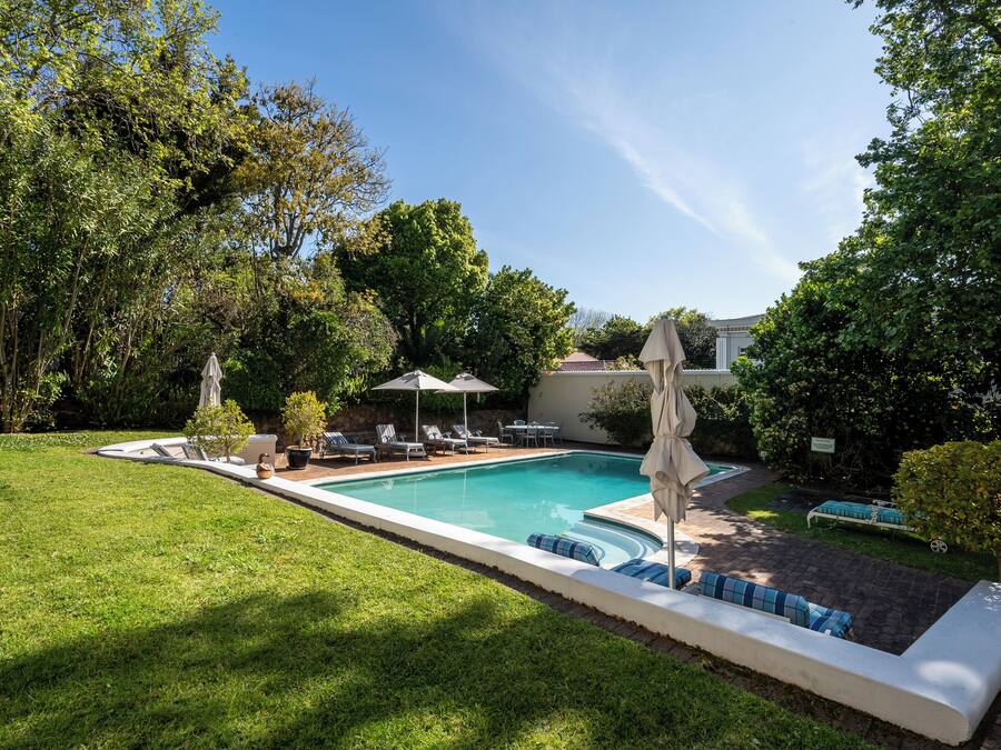 Piscina com espreguiçadeiras e guarda-sóis, cercada por um gramado bem cuidado e árvores.