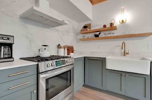 Eine Küche mit Gaskochfeld, Backofen und integriertem Spülbecken. Über dem Spülbecken befinden sich Holzregale und auf der Arbeitsfläche steht eine Kaffeemaschine.