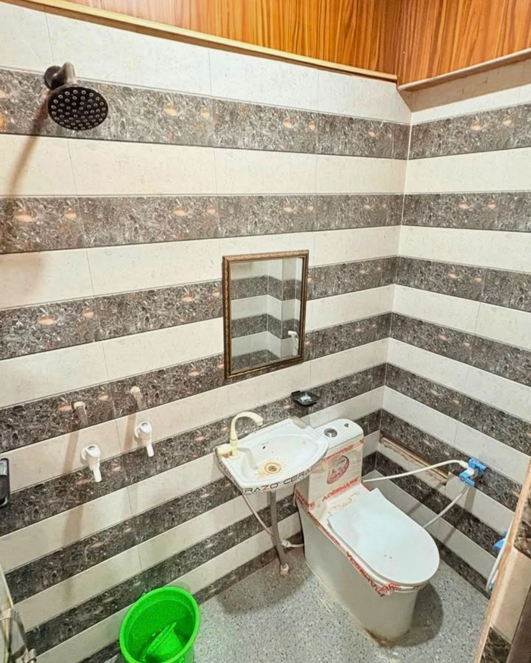 A bathroom with a shower, sink, mirror, toilet, and a green bucket.