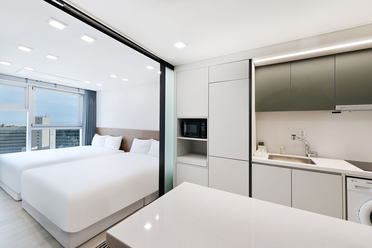Una habitación de hotel moderna con una cama grande, kitchenette y vistas a la ciudad.