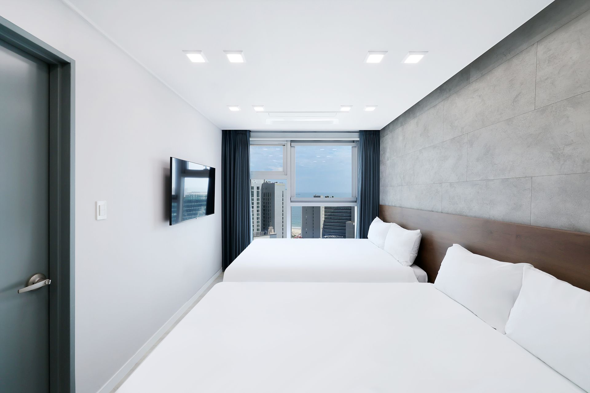 Habitación de hotel moderna con una cama grande, un televisor de pantalla plana en la pared y vista a la ciudad por la ventana.