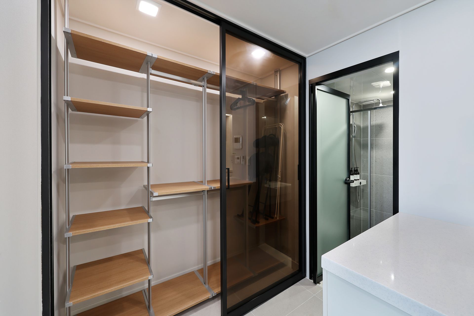 Un baño moderno con cabina de ducha de vidrio, encimera blanca y estantería empotrada con baldas de madera.