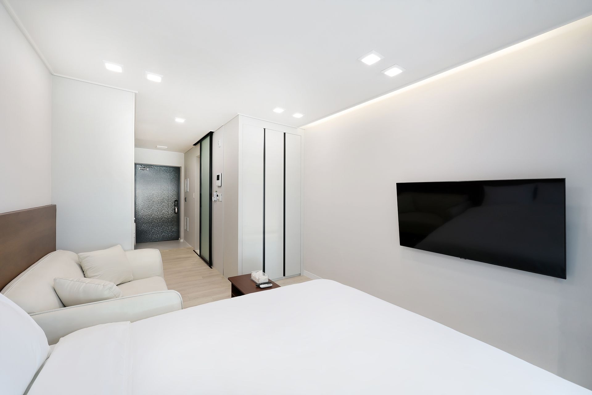 Una habitación de hotel moderna con una cama grande, un televisor de pantalla plana montado en la pared y una puerta corredera que da a un baño.