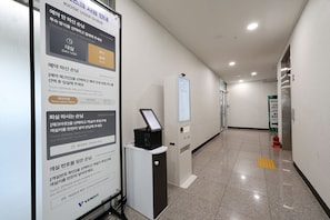 A hotel corridor with a check-in kiosk, a digital display for room selection, and a fire extinguisher. - Avenue The Solid (Busan)