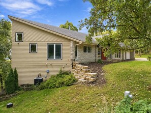 A two-story house with a sloped roof, a small front yard, and a stone staircase leading to the front door. - The Architect’s Overlook | Sweeping Valley Views (Galena)