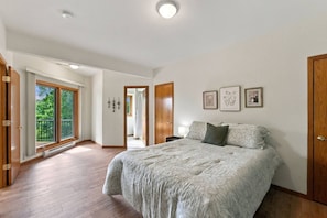 Une chambre avec un grand lit, une porte-fenêtre coulissante donnant sur un balcon et une vue sur la verdure.