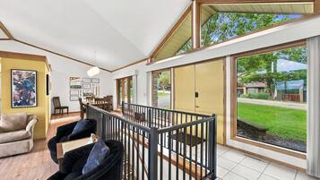 A spacious living room with a high ceiling, a dining area, and large sliding glass doors leading to a backyard.