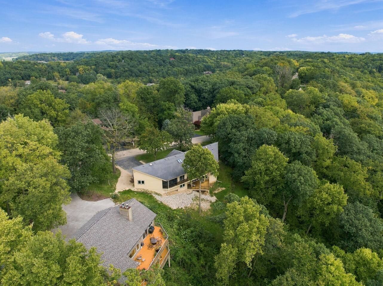 A residential property surrounded by dense forest, featuring a main house with a large deck and a separate building with a sloped roof.