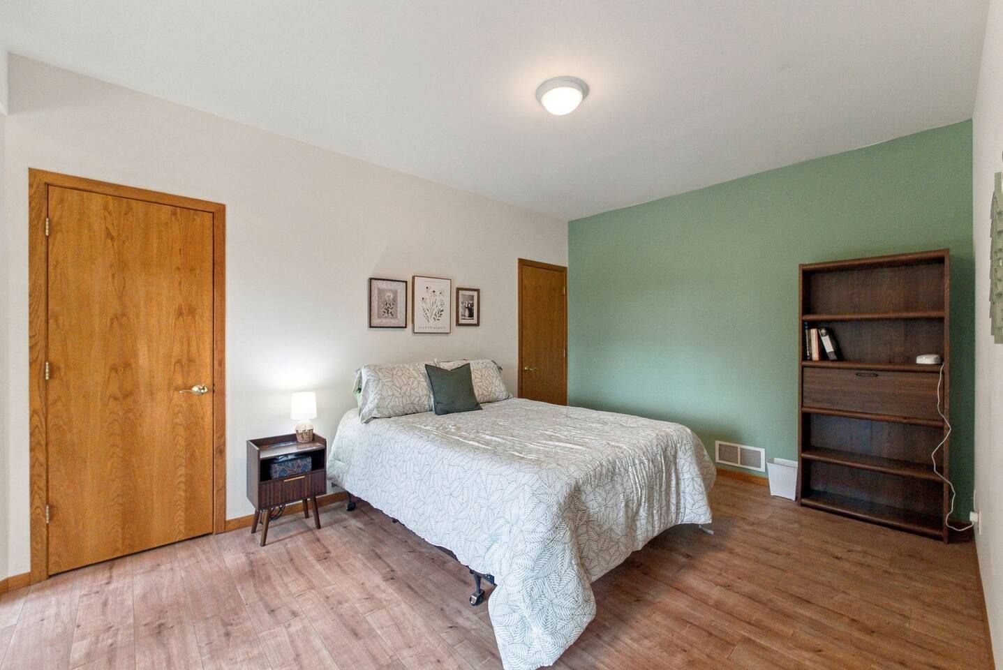 A bedroom with a bed, a nightstand, a bookshelf, and a door.