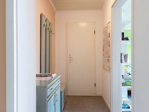 A narrow hallway with a white door, a dresser with drawers, and a shelf with books and a small collection of items. - Apartment Meyer by Interhome (Raben Steinfeld)