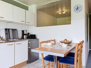 Cuina compacta amb armaris blancs, una cafetera i una taula de dinar amb caires blaus.