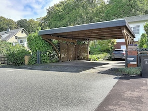A covered parking area with a gravel surface, a wooden pergola structure, and a building with a visible address sign. - Apartment Meyer by Interhome (Raben Steinfeld)