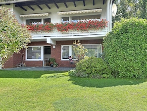 A two-story building with a balcony adorned with red flowers, a brick facade, and a well-maintained lawn. - Apartment Meyer by Interhome (Raben Steinfeld)