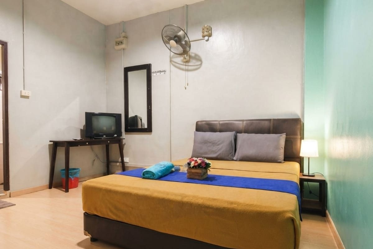 A hotel room with a bed, a television, a mirror, and a wall-mounted fan.