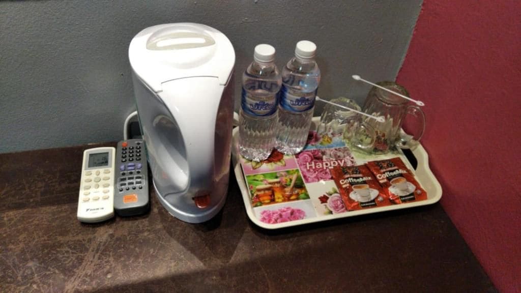 A coffee maker, two bottles of water, a tray with coffee packets, and a remote control on a table.