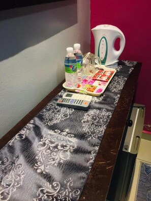 A table with a patterned tablecloth, a remote control, a tray with water bottles, a kettle, and a magazine. - Ghazrins Hotel Dataran Larkin (Taman Dataran Larkin)