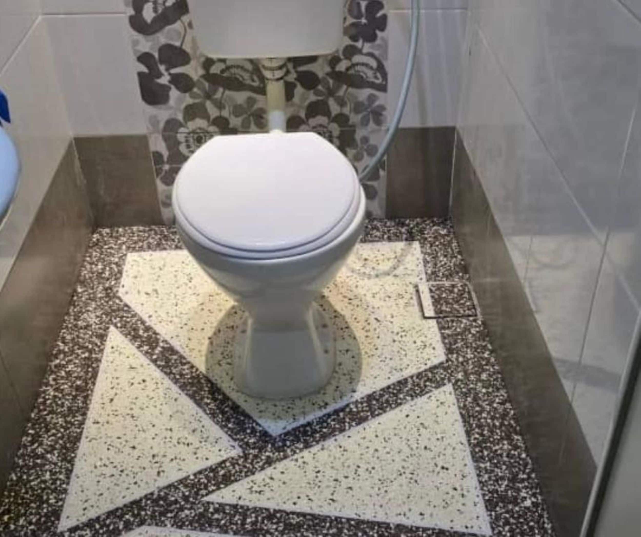 A toilet with a white lid in a bathroom with a speckled floor and a floral-patterned wall.