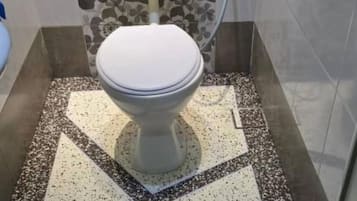 A toilet with a white lid in a bathroom with a speckled floor and a floral-patterned wall.