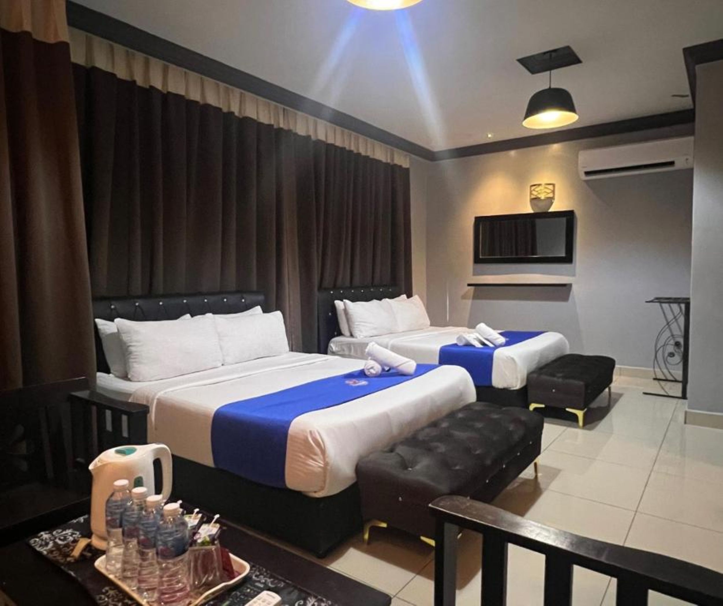 Habitación de hotel con dos camas, un escritorio con un descansamos para botellas de agua y un pequeño rincón de descanso.