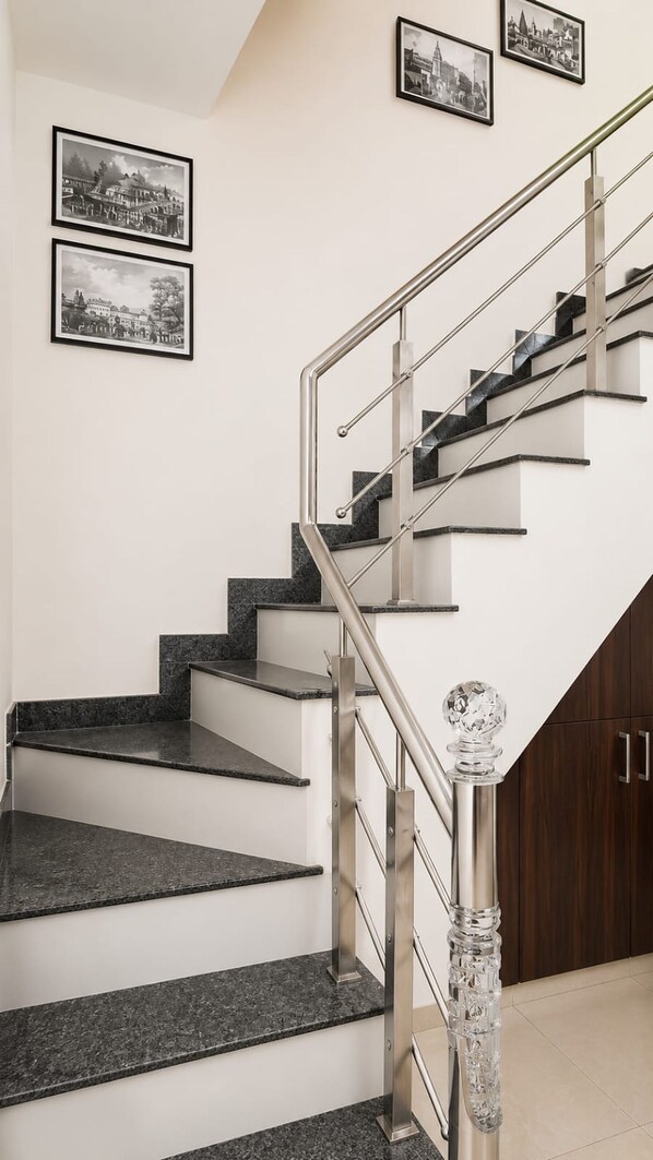 A staircase with a glass balustrade, a crystal balustrade ornament, and three framed black-and-white photographs on the wall. - Hotel MB Grand (Varanasi)