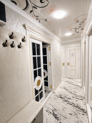 A hallway with a marble floor, white walls with gold trim, and a door with a decorative glass panel.