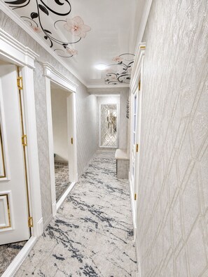 A hallway with marble flooring, white walls, and decorative ceiling artwork.