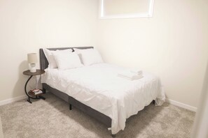 A neatly made bed in a room with a small bedside table, a lamp, and a power outlet. - Luxury Private Suite, Near Calgary Airport (Calgary)