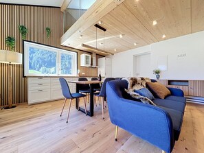 A modern living room with a blue sofa, wooden flooring, and a dining area with a wooden table and chairs. - Apartment Inari by Interhome (Gortipohl)