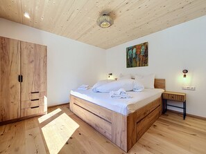 A bedroom with a wooden bed, a wardrobe, a bedside table, and a wall-mounted light fixture. - Apartment Inari by Interhome (Gortipohl)