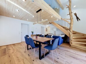 A modern interior with a wooden dining table, blue chairs, a staircase with a natural wood design, and a white wall. - Apartment Inari by Interhome (Gortipohl)
