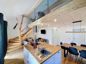 A modern kitchen with a wooden island, a dining area with a table and chairs, and a staircase with a wooden railing. - Apartment Akira by Interhome (Gortipohl)