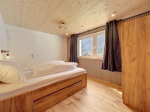 A bedroom with a wooden bed, a window with curtains, and a view of the outdoors. - Apartment Laika by Interhome (Gortipohl)