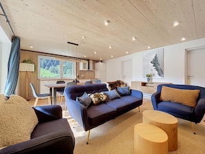 Ein modernes Wohnzimmer mit einem dunkelblauen Sofa, einem runden Holztisch und einem großen Fenster mit Blick auf eine grüne Landschaft.
