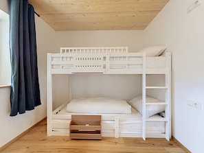 A bunk bed with a wooden ladder, a small wooden drawer, and a window with curtains. - Apartment Laika by Interhome (Gortipohl)