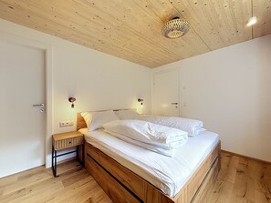A bedroom with a wooden bed, a nightstand, a wall-mounted light, and a ceiling light fixture.