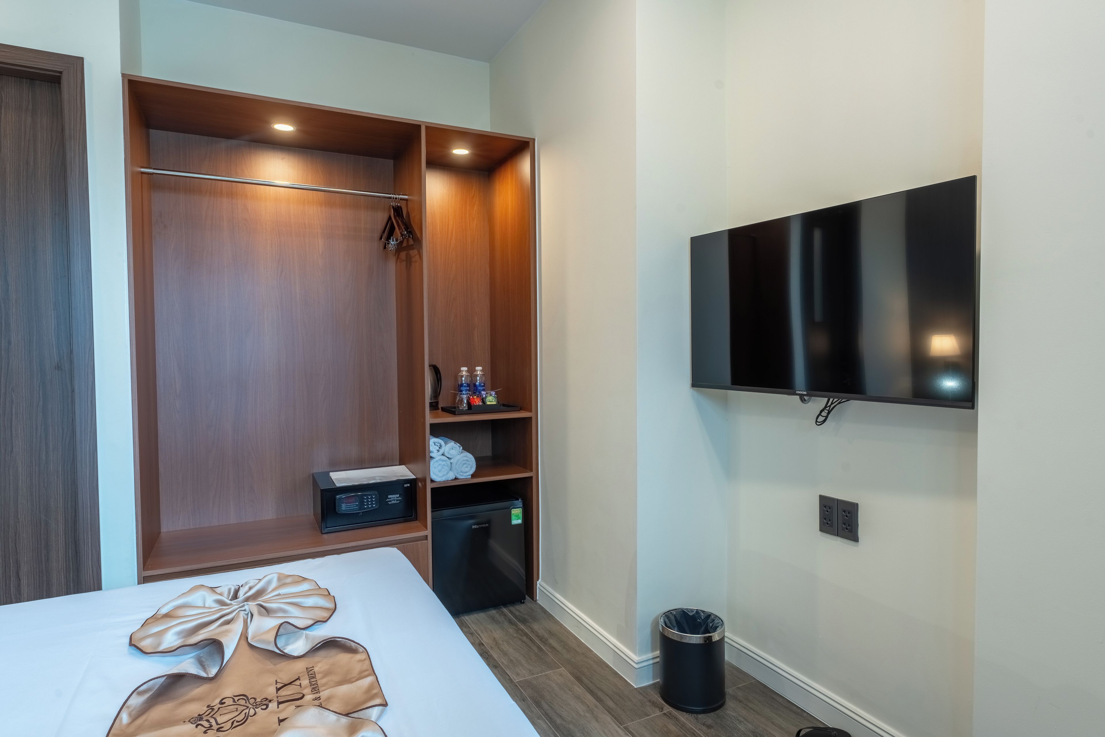 A hotel room with a bed, a wardrobe, a minibar, a television, and a trash bin.