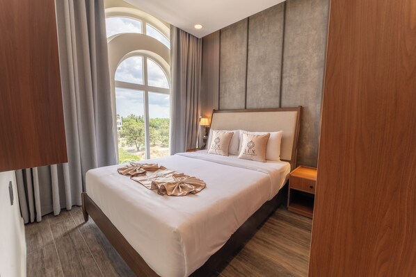 A hotel room with a large bed, a nightstand, a lamp, and a view of the outdoors.