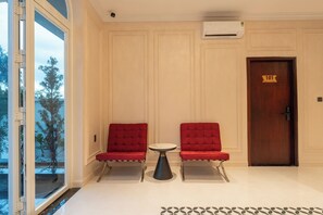 A hotel lobby with two red upholstered chairs, a small round table, and a wooden door with a room number.