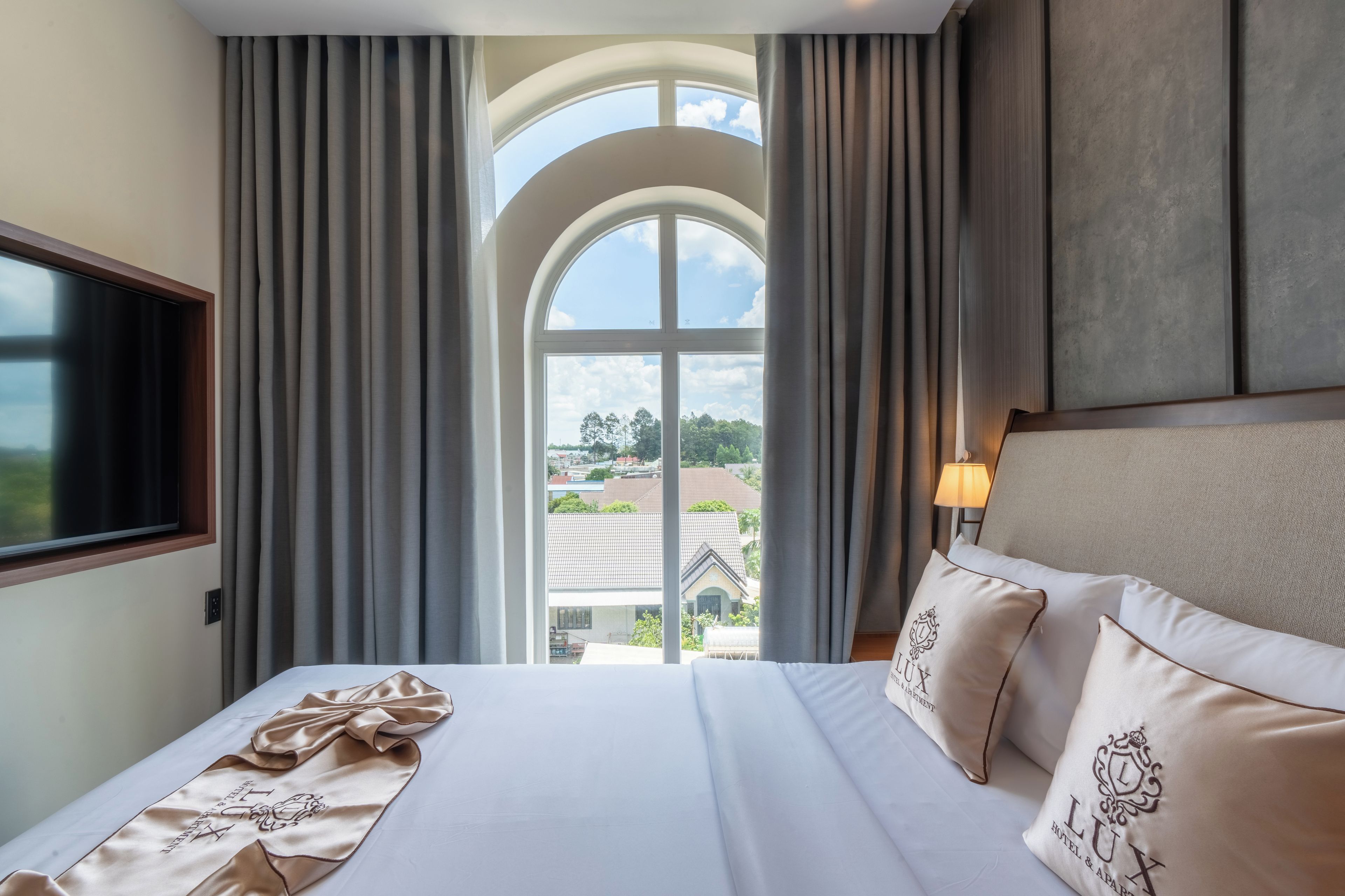 Habitación de hotel con una cama grande, televisor y vista a una zona residencial por una ventana.