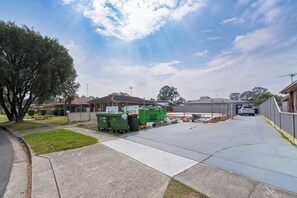 A parking area with a fence, green dumpsters, and a building with a sign. - Be Dahlia by Esteem Retreats (Quakers Hill)