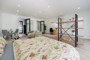 A modern bedroom with a bed, a desk, and a chair. There is a window with blinds and a plant on the desk.