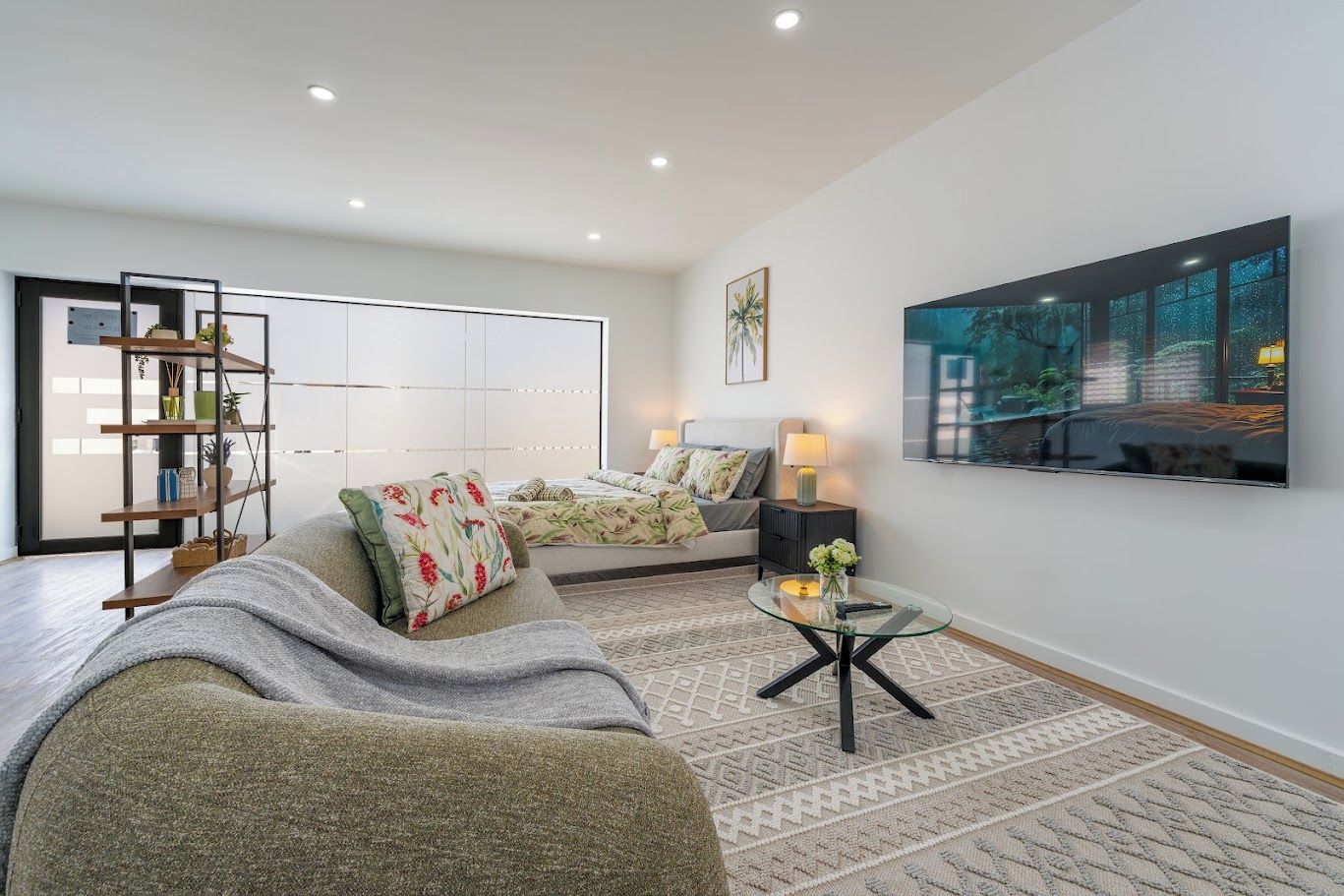 A modern living room with a sofa, a bed, a coffee table, and a large painting on the wall.