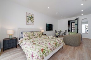 A bedroom with a bed, bedside tables, a TV, a small table with chairs, and a large mirror. - Be Dahlia by Esteem Retreats (Quakers Hill)