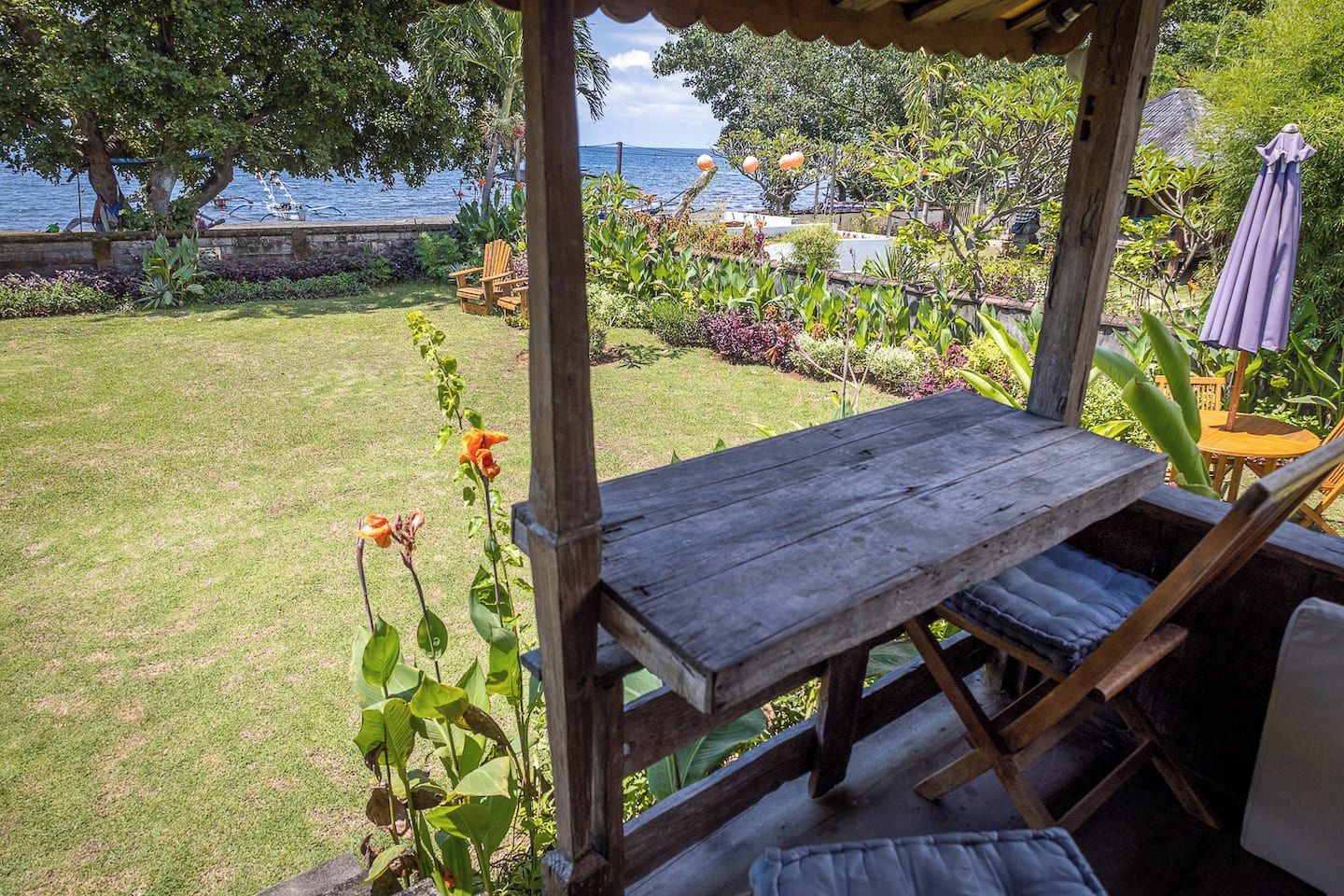 Ett träbord och stolar under en pergola, med utsikt över en välskött gräsmatta och en vattenyta.
