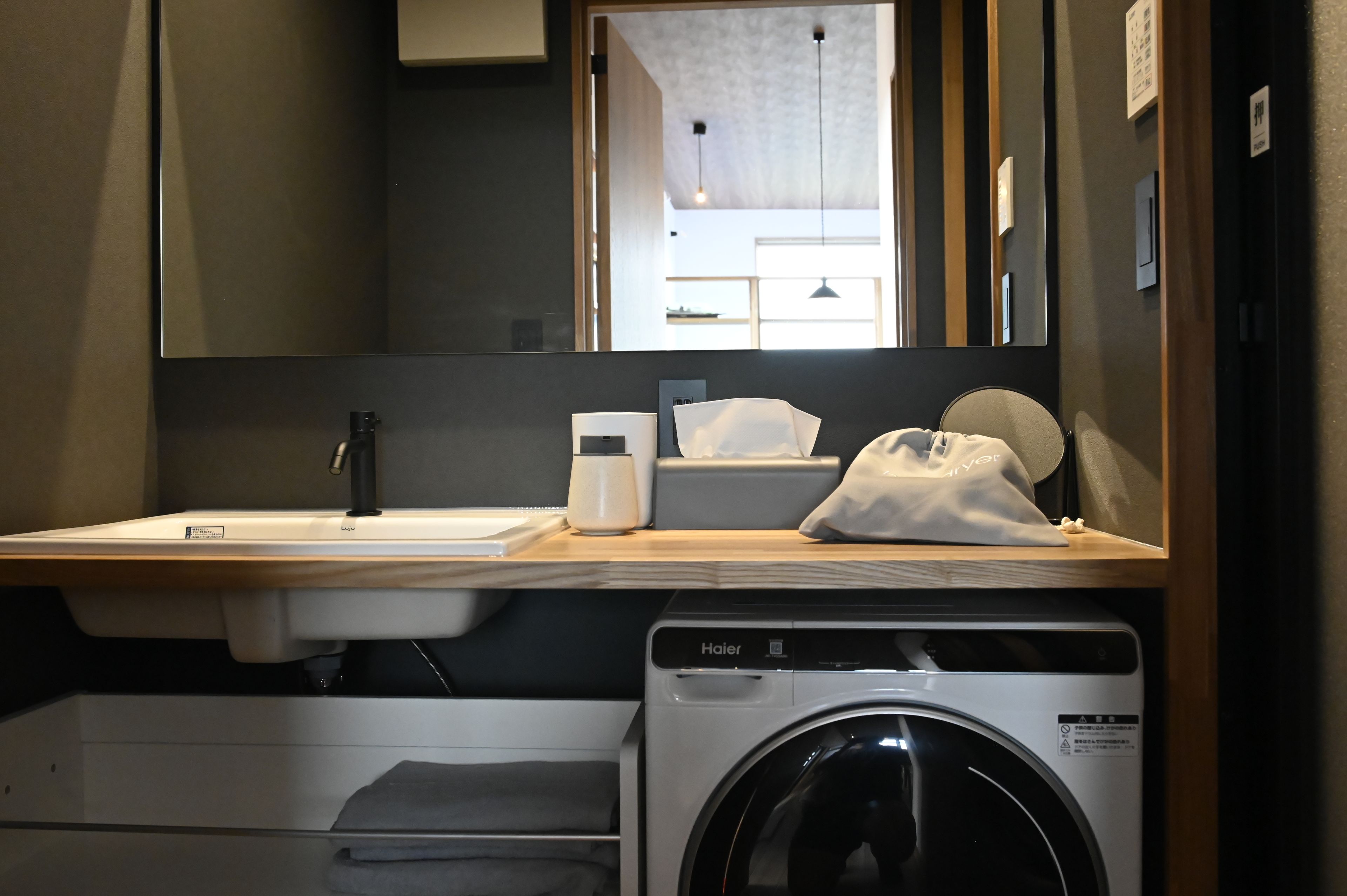 A hotel bathroom with a sink, mirror, towel dispenser, and a washing machine.