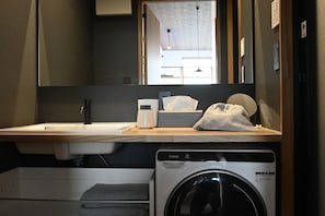 Un bany d'hotel amb un rentapins, un mirall, un dispensador de tovalloles i una màquina de rentar.
