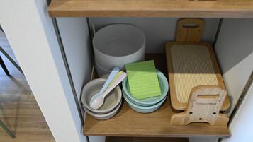 A kitchen shelf with a grey bowl, a green sponge, a wooden cutting board, and a wooden utensil holder.