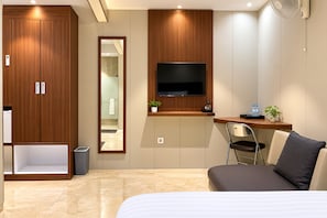 A modern hotel room with a bed, a desk with a chair, a TV, and a wardrobe. - 555 Nangka Guest House (Jakarta Selatan)