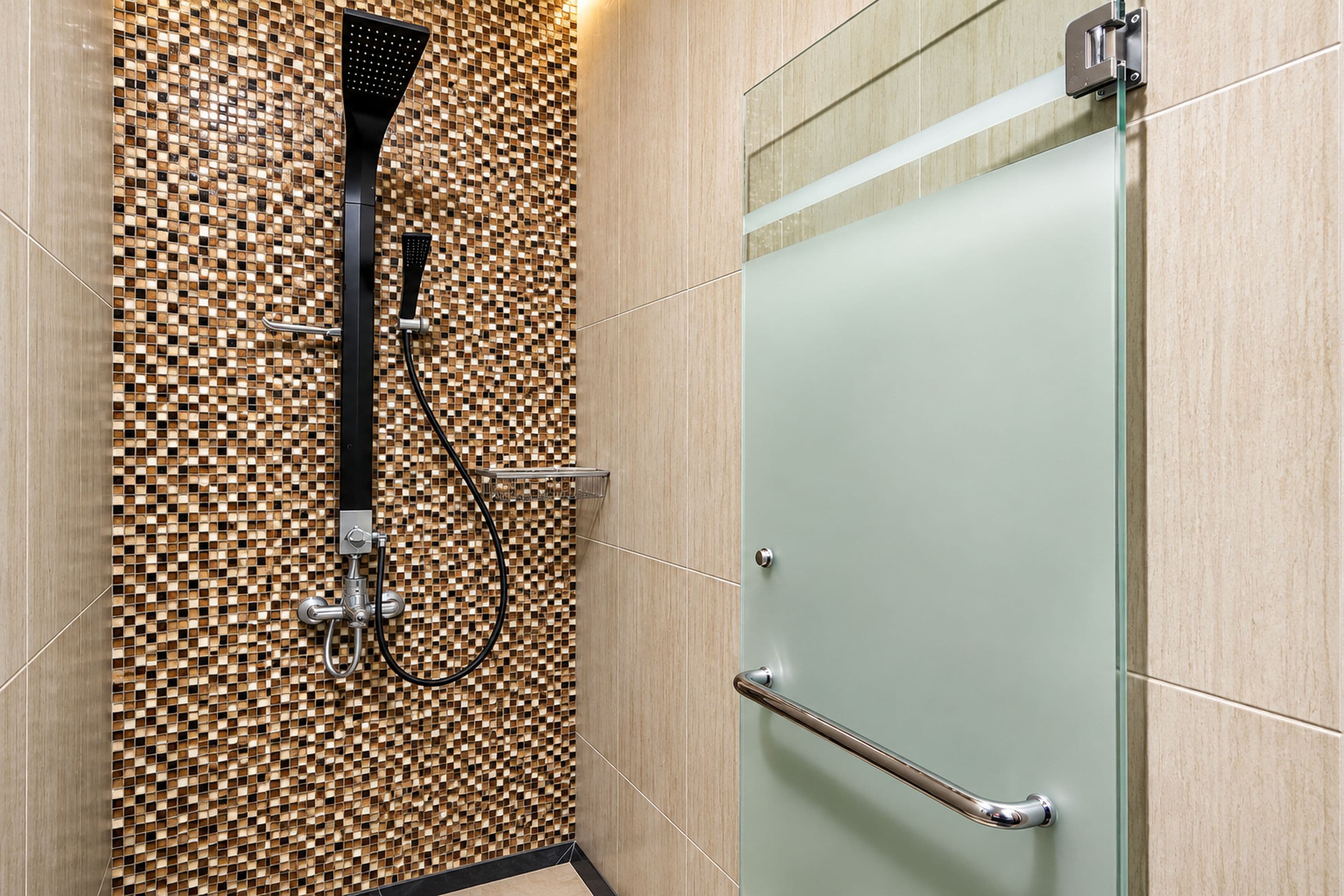 A modern shower area with a mosaic tile wall, a glass door, and a metal handrail.
